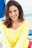 A brunette woman on a beach wearing a yellow knitted jumper