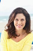 A brunette woman on a beach wearing a yellow knitted jumper