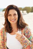 Brünette Frau in weißem Shirt und bunter Strickjacke am Strand