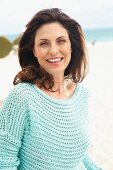 Brünette Frau in mintfarbenem Lochstrickpulli am Strand