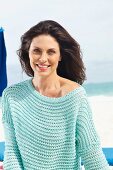 A brunette woman on a beach wearing a mint-coloured, openwork jumper