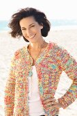 A brunette woman on a beach wearing a white top and colourful cardigan