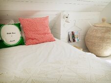 Rustic, white, attic bedroom with crocheted bedspread, scatter cushions and large basket