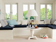 Window seat with black seat cushion and patterned scatter cushions in renovated, white, country-house interior