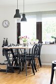 Black Thonet chairs around dining table below pendant lamps with black lampshades next to window