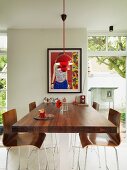 High, walnut table abutting wall and bar stools with wooden shell seats below red pendant lamps and between French windows