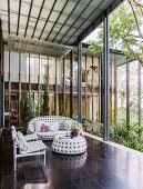 White, modern outdoor furniture on terrace with dark tiled floor in front of glass facade