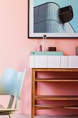 Black-framed picture above open shelves in retro interior with pastel pink wall