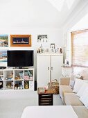 Gemütliche Wohnzimmerecke mit vollgestelltem offenen Regal, Fernseher und gerahmten aufgestellten Familienfotos