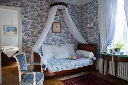 Antique sleigh bed with canopy against white and blue toile de jouy wallpaper
