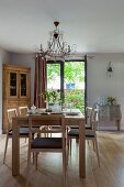 Pale wooden chairs and table in front of rustic corner cabinet next to French windows