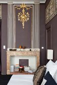 Disused marble fireplace below gilt stucco element on wall in corner of living room