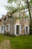 Rustic stone country house with white shutters and window in summer garden