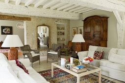 Pale sofa set and coffee table in living room in renovated country house with whitewashed wood-beamed ceiling