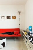 Red designer sofa next to fitted, half-height shelves in contemporary interior