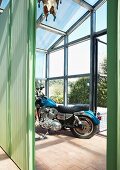 Blaues Motorrad im Glashaus mit grünem Raumteiler