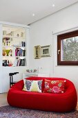 Rote Designercouch mit gemusterten Kissen in Wohnzimmerecke mit weißem Raumteilerregal