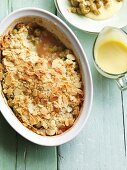 Gooseberry crumble in a baking dish with vanilla sauce