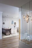 Ornate sconce lamp on mirrored wall; black kitchen counter and loose-covered chairs in background