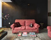 Traditional sofa with brocade pattern against black stucco lustro wall and coffee table with glass top and curved metal frame in foreground