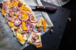 A vegetable pizza with red onions and walnuts