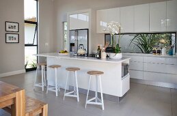 Island counter with bar stools and pale fitted kitchen in open-plan interior