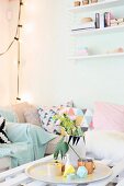 Scatter cushions with graphic patterns on sofa in corner behind vase and paper decorations on tray on coffee table