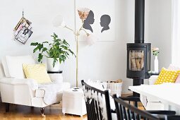 Dining area with black chairs, log burner and antique armchair with pale cover next to retro standard lamp