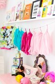 Toys on top of pale chest of drawers below string of colourful tassles and pictures on shelf