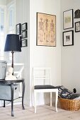 Weiß lackierter Stuhl mit schwarzem Sitzpolster vor Wand in Zimmerecke, oberhalb gerahmte Bilder