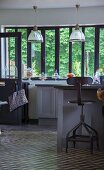 Vintage Drehstuhl vor Küchentheke, im Hintergrund Fensterband mit dunkelgrau lackierten Rahmen und Gartenblick