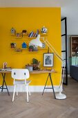 Tabletop on metal trestles against yellow wall, white-painted retro chair and modern standard lamp to one side