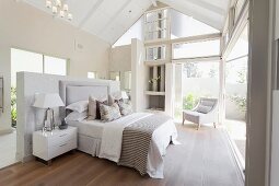 Double bed with tall upholstered headboard and bedside cabinet against half-height partition in bedroom of contemporary house