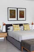 Symmetrical bedroom in shades of grey; scatter cushions with graphic pattern on box-spring bed below two artworks on wall