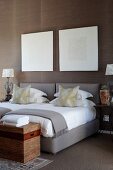 Graphic art above twin beds with grey upholstered frames, elegant scatter cushions and trunk at foot