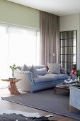 Organically shaped wooden side table next to elegant sofa in front of glass wall with floor-to-ceiling curtain