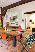 Rustic, modern dining table and retro chairs on terracotta floor below old, exposed wooden beams