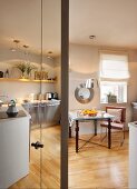 Interessanter Stilmix in Wohnküche mit Edelstahlfronten und künstlerischer Tischkonstruktion aus verstrebten Antikfüssen mit Glasplatte