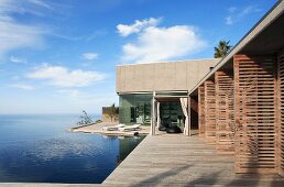 Zeitgenössisches Wohnhaus mit offenen Terrassentüren aus Holzlamellen und umlaufende Terrasse, seitlich Infinity Pool mit nahtlosem Blick auf das Meer