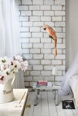 Detail of rustic room; parrot figurine in front of concrete block wall, books on small stool used as bedside table on white board floor