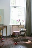 Patterned fabric and cushions on two wooden chairs below lattice window with grey, floor-length curtain to one side