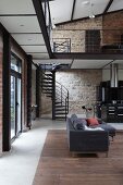 Couch in front of black spiral staircase against stone wall in loft apartment