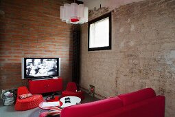 Red furniture in corner of room with exposed masonry walls and TV on metal sideboard