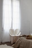 White Ron Arad armchair between floor-length curtains and bed