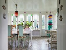 Turquoise-painted, wooden chairs with carved backrests at white dining table in rustic dining room with row of stained-glass windows