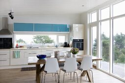 Pale kitchen counter and dining area with white chairs around wooden table in open-plan kitchen