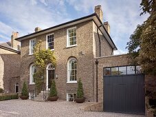 English house with brick facade, arched windows with white lattice frames on ground floor, narrow steps leading to front door and gravel front courtyard