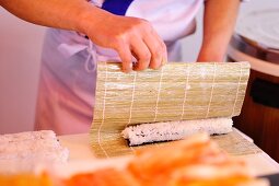 Sushi zubereiten: Reis in Bambusmatte zusammenrollen