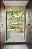 Open French windows painted green leading onto summery courtyard terrace; dark brown fitted cupboards with metal door fittings in foreground