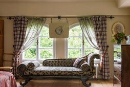 Antique chaise longue with ikat upholstery in front of arched windows with gathered curtains
